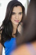 Hispanic woman applying lipstick in mirror
