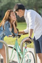 Korean couple locking bicycle to rack in park