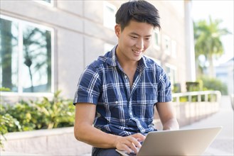 Korean man using laptop outside building