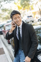 Korean businessman talking on cell phone near car