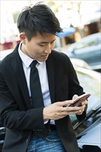 Korean businessman using cell phone near car