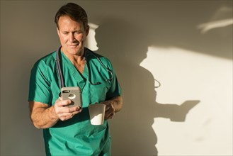 Caucasian nurse using cell phone casting shadow on wall