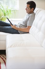 Hispanic man using digital tablet on sofa