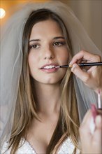 Caucasian stylist applying makeup on bride