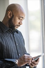 Black man using cell phone near window