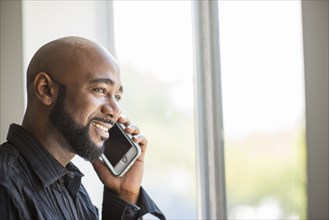 Black man talking on cell phone near window