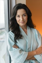 Hispanic woman wearing bathrobe at window