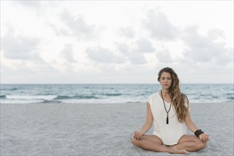 Hispanic woman meditating on beach