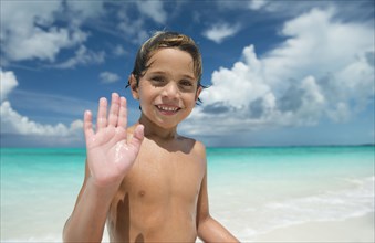 Hispanic boy waving on beach