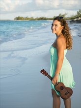 Hispanic teenage girl holding ukulele on beach