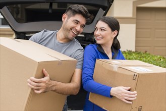 Hispanic couple carrying cardboard boxes near car