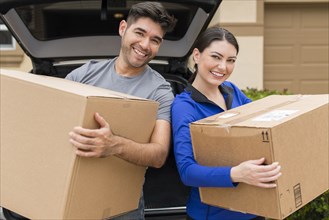 Hispanic couple carrying cardboard boxes near car