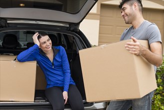 Hispanic couple carrying cardboard boxes near car