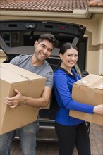 Hispanic couple carrying cardboard boxes near car