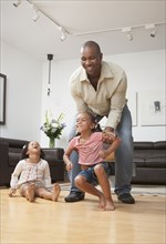 African American father playing with daughters in living room