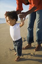 African mother helping son walk in beach