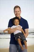 Father holding mixed race son at beach