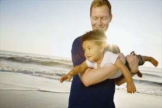 Father playing with mixed race son at beach