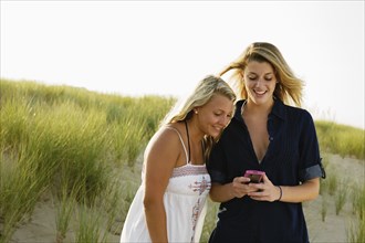 Smiling teenage girls text messaging with cell phone on beach