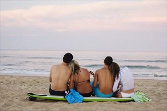 Teenage couples sitting on surfboard on beach