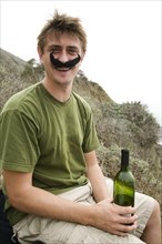 Caucasian man in costume mustache holding wine bottle