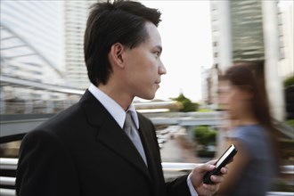 Asian businessman text messaging on cell phone outdoors