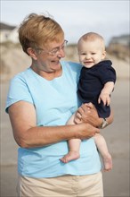 Smiling Caucasian grandmother holding grandson on beach