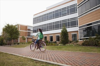 Caucasian student riding bicycle on campus