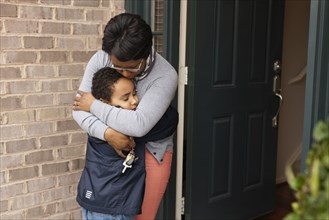Mother hugging son at front door