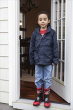 Mixed race boy wearing rainboots and jacket