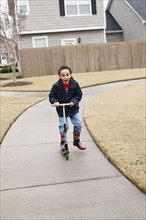 Mixed race boy playing on scooter on suburban street