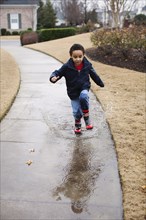 Mixed race boy splashing in rainboots