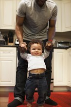 Father helping baby walk in kitchen