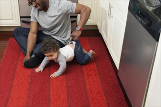 Father helping baby crawl in kitchen