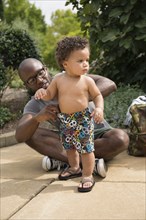 Father adjusting toddler son's shorts in park