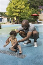 Father and toddler son playing in fountain
