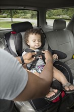Father buckling toddler son into car seat