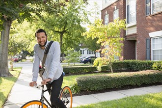 Mixed race man on bicycle on suburban sidewalk