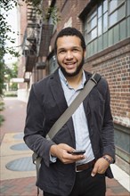 Mixed race businessman using cell phone on city sidewalk