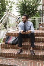 Mixed race businessman using cell phone on front stoop