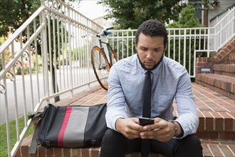 Mixed race businessman using cell phone on front stoop