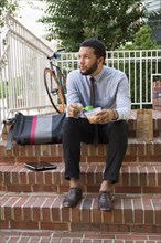 Mixed race businessman eating on front stoop