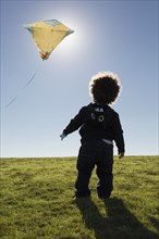 Mixed race boy watching kite flying against blue sky