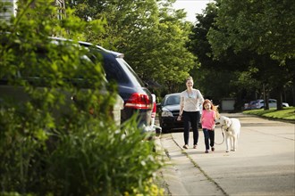 Caucasian mother and daughter walking dog on suburban street