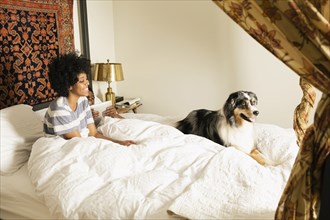 Mixed race woman sitting with dog in bed