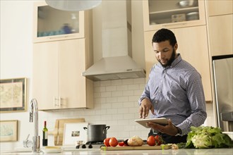 Mixed race man cooking with tablet computer in kitchen