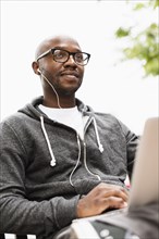 Black man using laptop and earphones outdoors