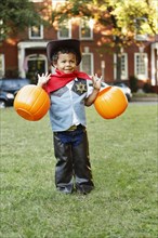 Mixed race boy in cowboy costume holding pumpkin pails on Halloween