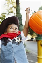 Mixed race boy dressed as cowboy holding pumpkin pail for Halloween