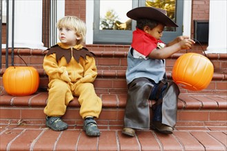 Boys in costumes trick sitting on front stoop on Halloween